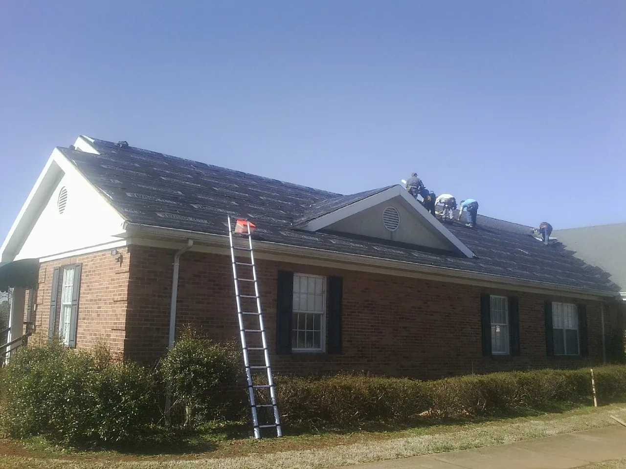 Crew tearing shingles off a brick ranch roof with a ladder set — Emergency Roof Repair work by our crew in Mayfield