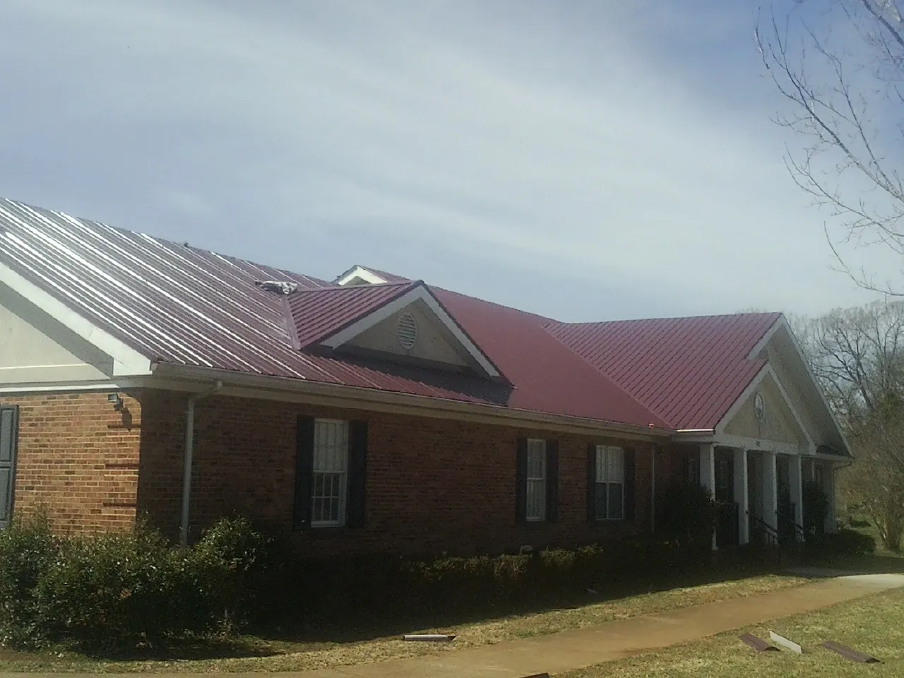 Red metal roof with gabled entries on a long brick building, from a Hail Damage Roof Repair job in Mayfield