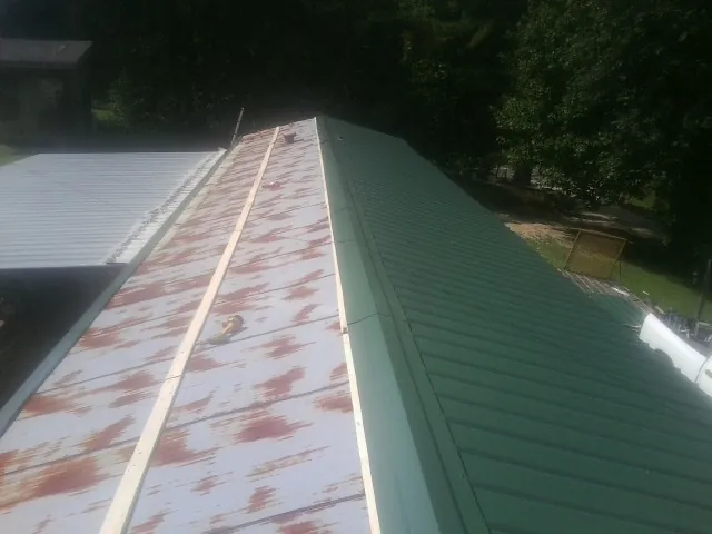 Old rusted panels beside newly installed green metal roofing — Wind Damage Roof Repair by Roofing Brothers in Mayfield