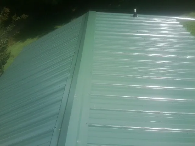New green metal panels meeting at the ridge of a roof — Flat Roof Repair work by our crew in Mayfield