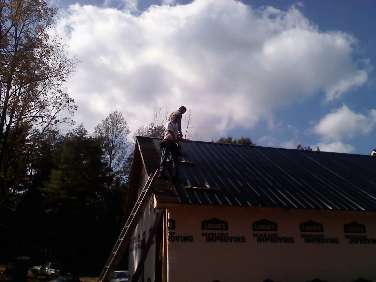 Roofer fastening dark metal panels high against a cloudy sky, from a Roof Inspection job in Mayfield