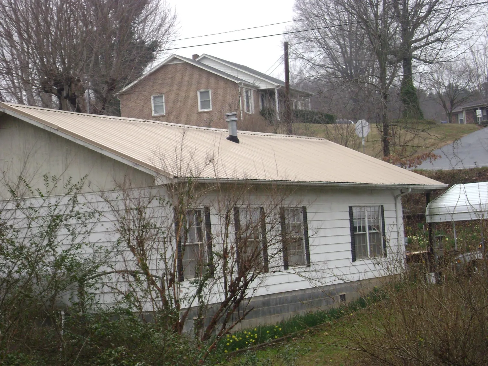 Tan metal roof on a white sided house set into a hillside — Commercial Roofing by Roofing Brothers in Mayfield